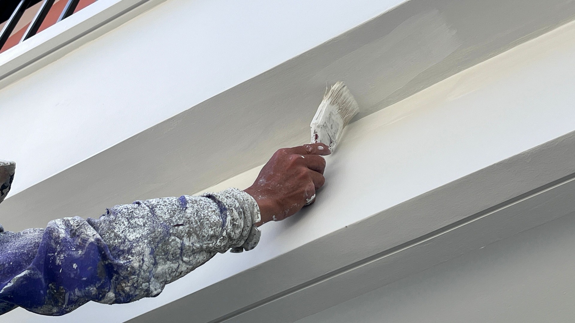 A worker is painting the walls of the house with a primer using a paint brush.